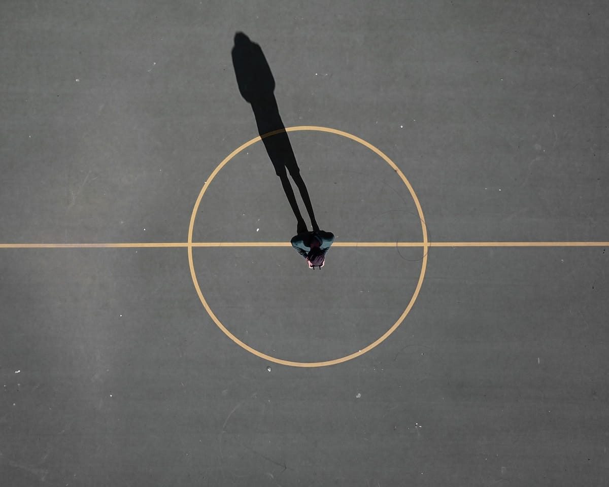 man stainding on black concrete floor casting shadow